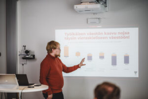Henkilö esittelee yleisölle diaa, joka on heijastettu seinälle.
